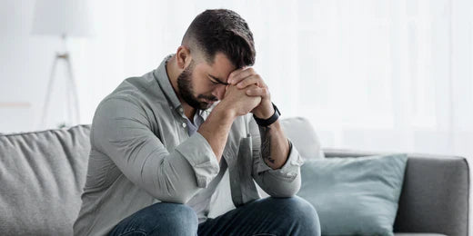 Man sat down looking upset, with his head in his hands.