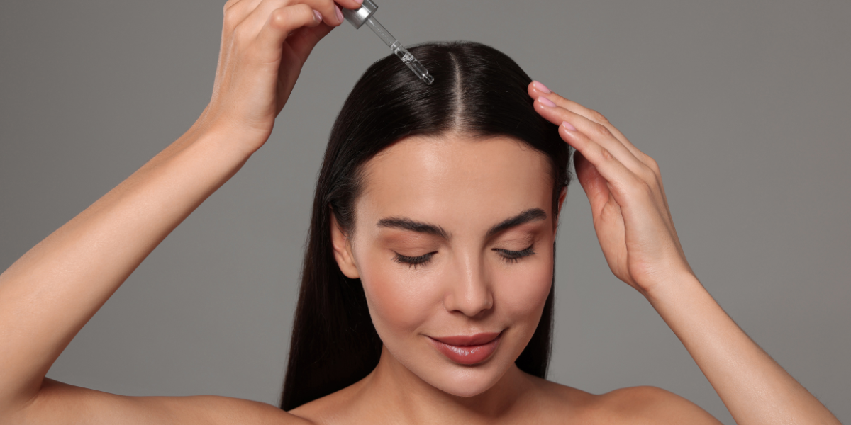 Woman using applicator to apply hair serum to the roots of her hair. 