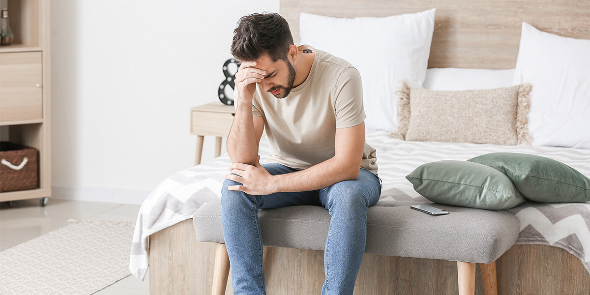 Man sitting on his bed looking depressed about his hair loss.