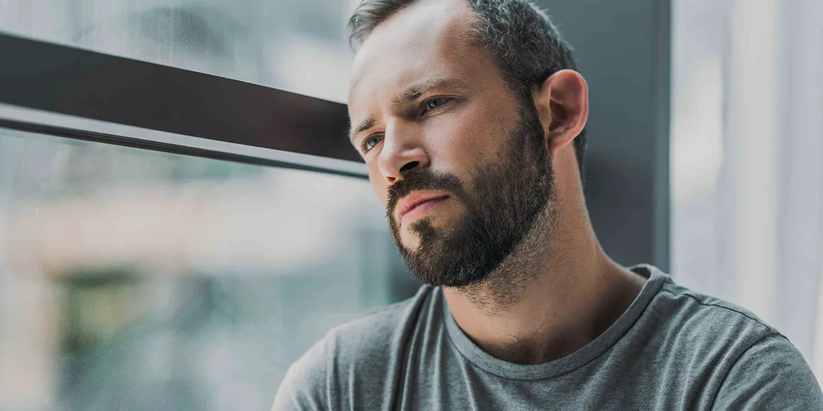 Man looking out window looking worried about post-finasteride syndrome.