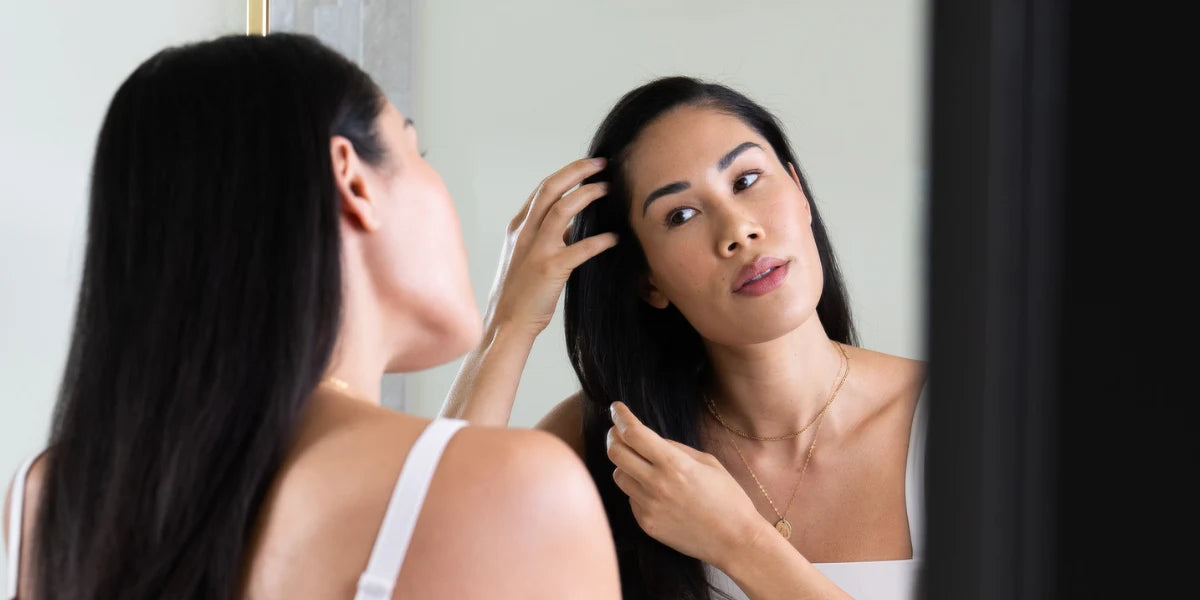 Young woman examining hair in mirror for signs of whether female hair loss is reversible.