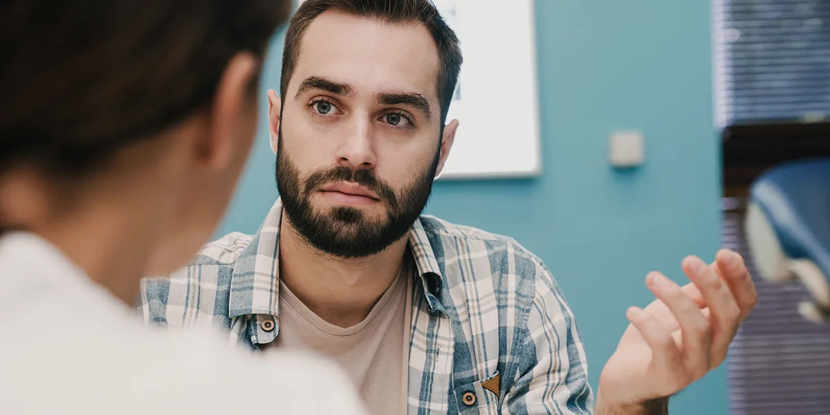 Young man discussing finasteride vs minoxidil with his doctor.