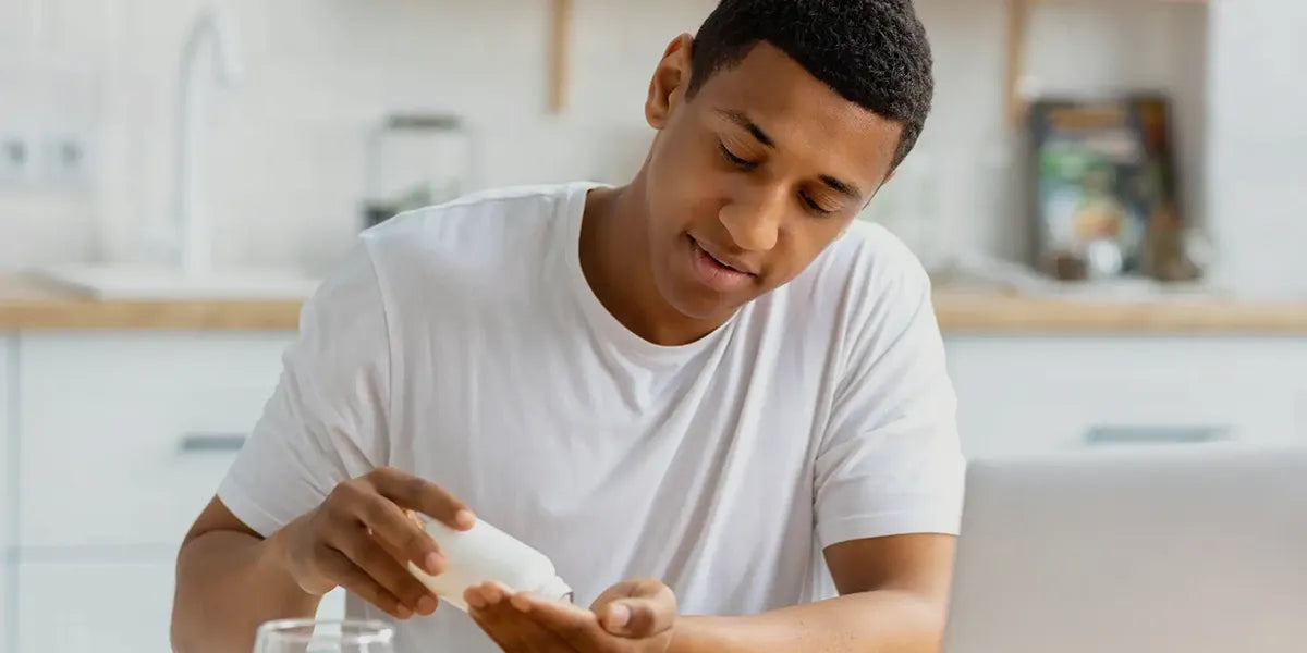 Young man taking dutasteride while researching dutasteride side effects on his laptop.