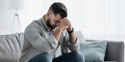 Man sat down looking upset, with his head in his hands. 