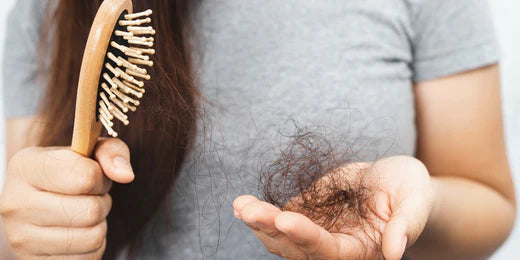 Woman holding brush in one hand and a clump of hair in the other, indicating hair shedding. 