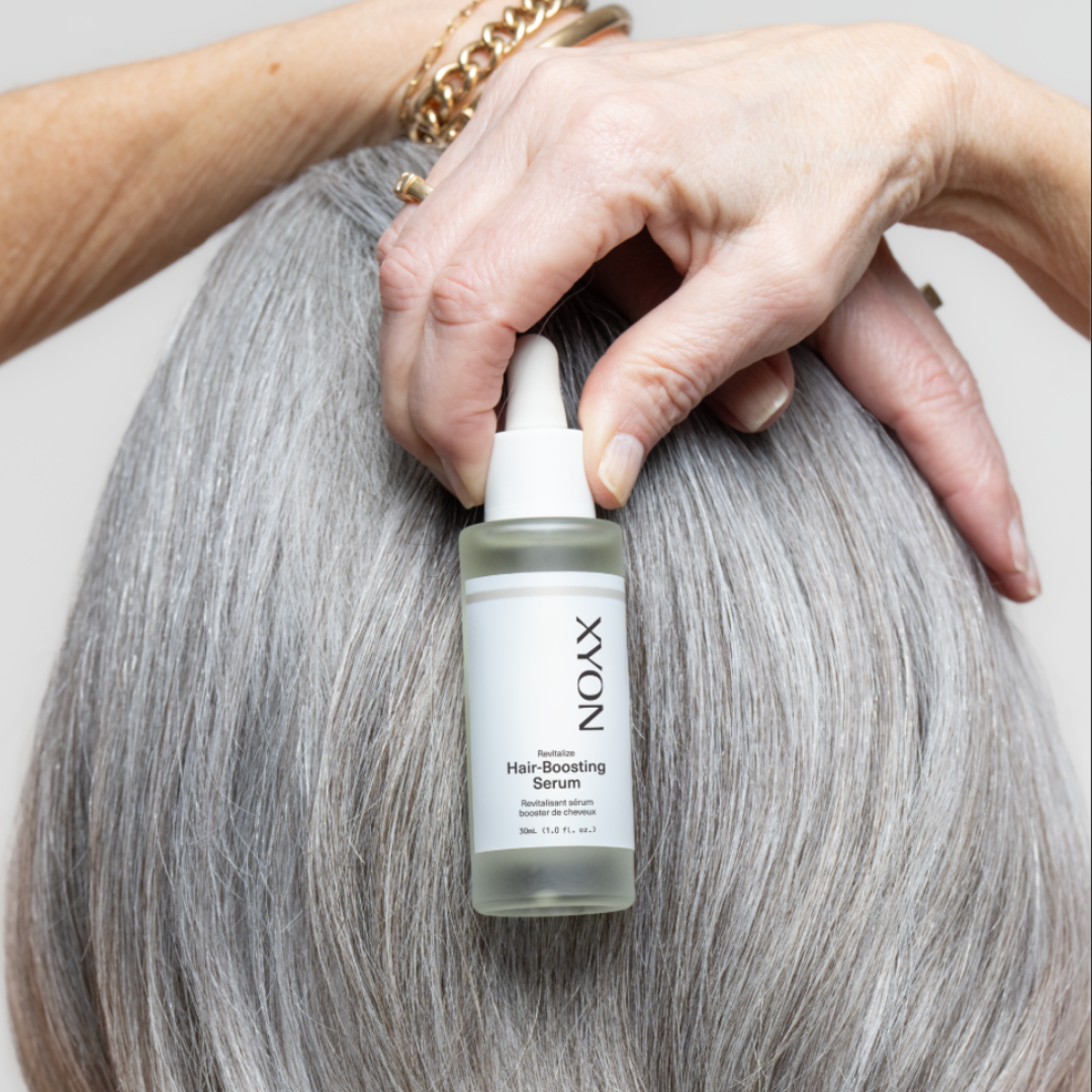 old woman with grey hair holding hair serum bottle