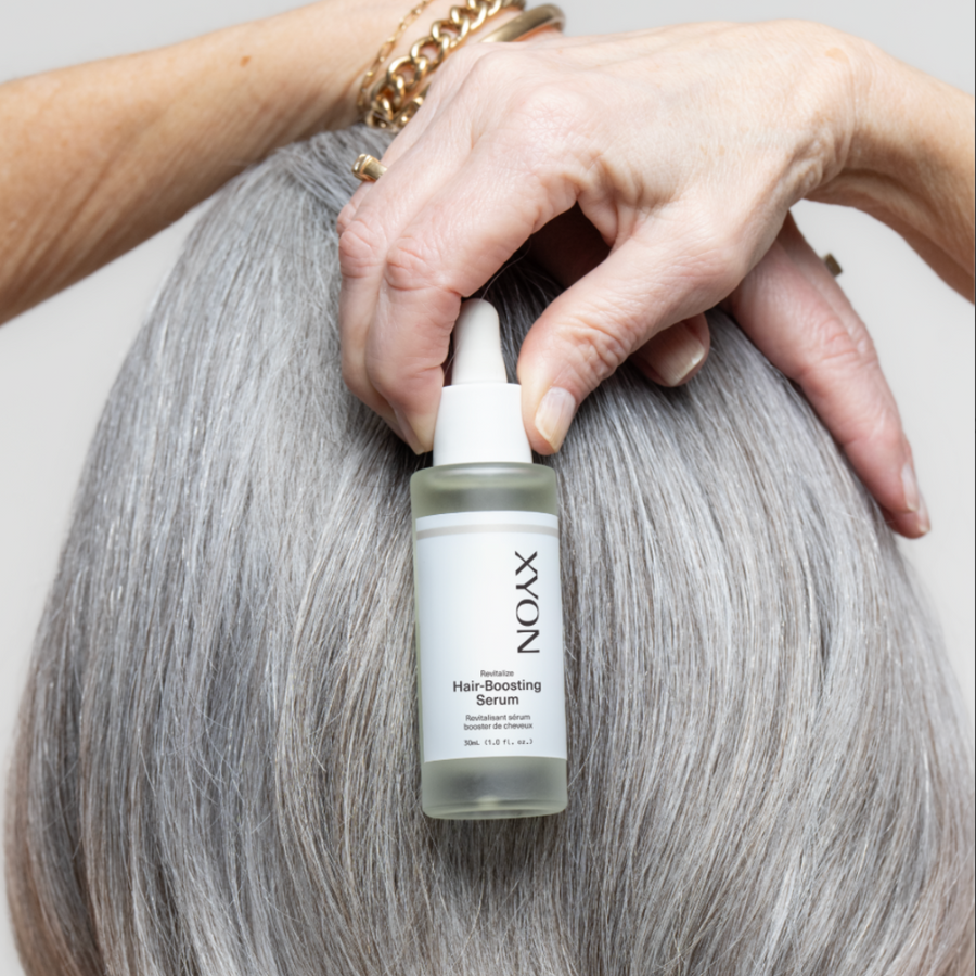 old woman with grey hair holding hair serum bottle